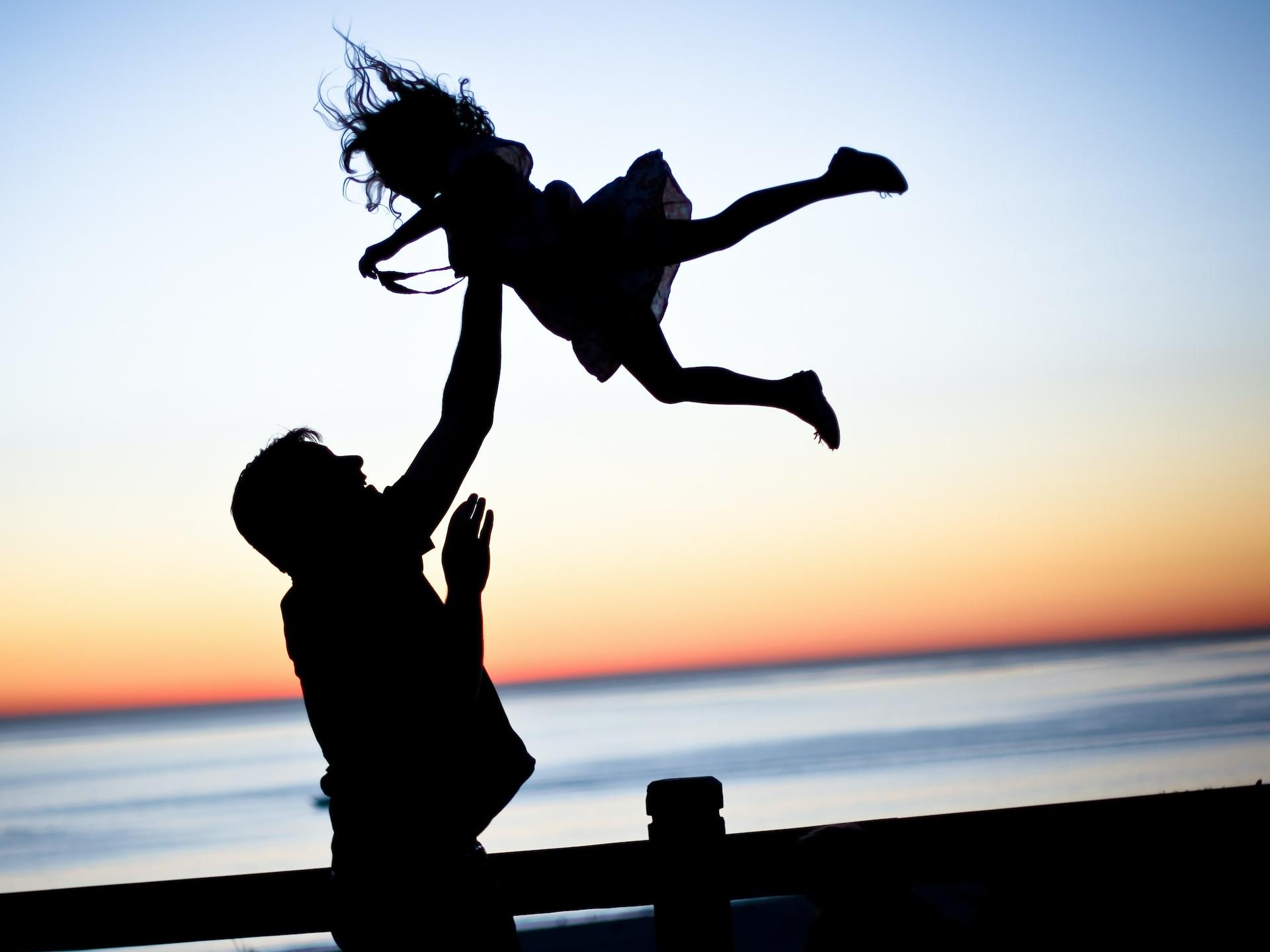 silhouette of man throwing girl in air